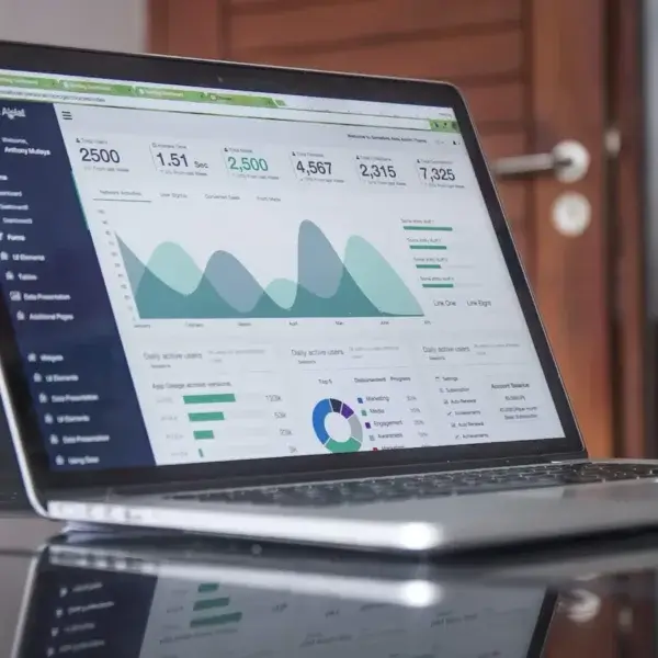 A laptop on a reflective table displays data analytics dashboards with charts, graphs, and statistics in blue and green tones—perfect for bookkeeping or accounting tasks. A partly open wooden door is visible in the background. - Victoria website design
